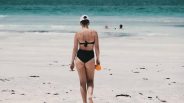 Siyah mayo giymiş genç bir kadın Cennet Sahili 'ndeki Turkuaz Okyanusu' na giriyor.