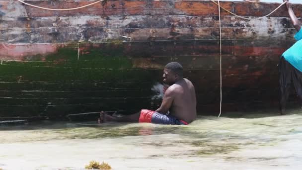 An African Fisherman Cleans a Boat from Algae on the Shore at Low Tide, Zanzibar — Stock Video