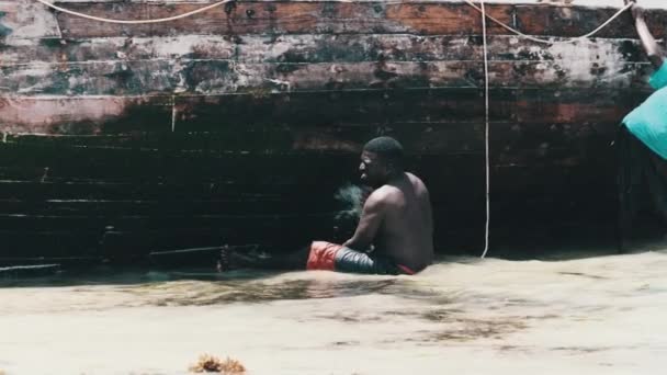 Seorang nelayan Afrika membersihkan perahu dari Algae di pantai di Low Tide, Zanzibar — Stok Video