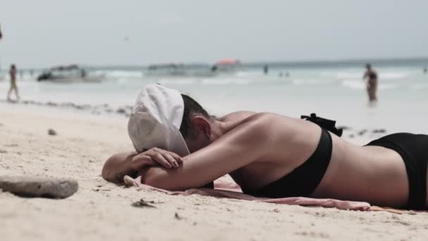 Mujer joven tomando el sol en una playa paradisíaca de arena acostada en bikini negro cerca del océano — Vídeos de Stock