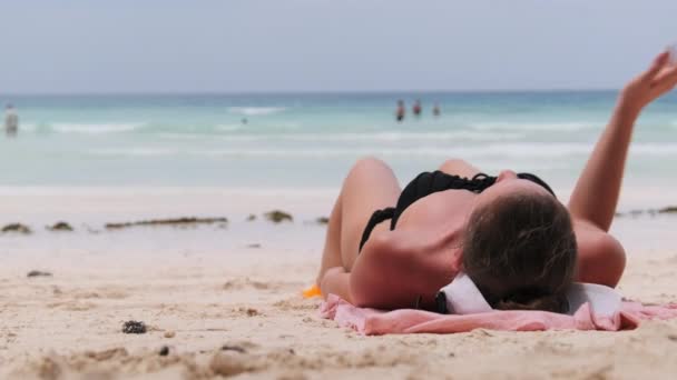 Młoda kobieta opala się na plaży Paradise Sandy Leżąc w czarnym bikini w pobliżu oceanu — Wideo stockowe