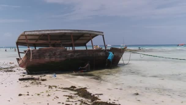 アフリカの漁師はザンジバルのロータイドで海岸の藻類からボートをきれいにする — ストック動画