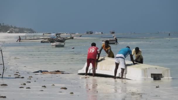 アフリカの漁師がザンジバルのロータイドにある海岸の藻類からボートをきれいにする — ストック動画