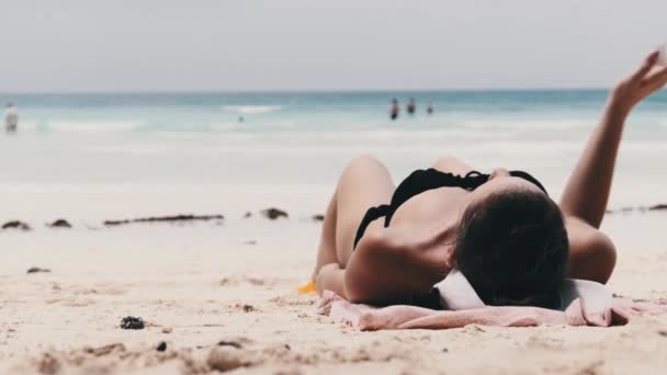 Genç Kadın Cennet 'te güneşleniyor Sandy Plajı' nda Okyanus kıyısında siyah bir Bikini 'de yatıyor — Stok video