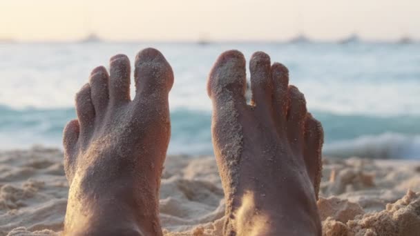POV πόδια του νεαρού άνδρα που βρίσκεται στην αμμώδη παραλία από τον ωκεανό κατά τη διάρκεια του ηλιοβασιλέματος, Ζανζιβάρη — Αρχείο Βίντεο