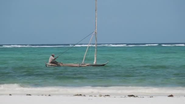 Afrikkalainen kalastaja vanhassa kuivassa puisessa veneessä, joka purjehtii valtamerellä korkealla vuorovedellä, Sansibar — kuvapankkivideo