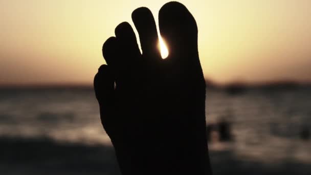 POV Silhouette of Feet of Young Man Lying on Sandy Beach by Ocean During Sunset — Stock Video