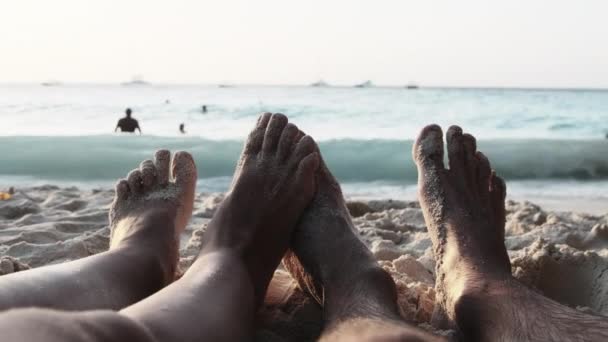 POV Feet of a Couple of Men and Women Leżący na piaszczystej plaży o zachodzie słońca nad oceanem — Wideo stockowe