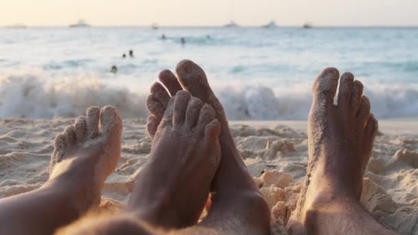 POV Jalat pari miestä ja naista makaa hiekkarannalla auringonlaskun Ocean — kuvapankkivideo