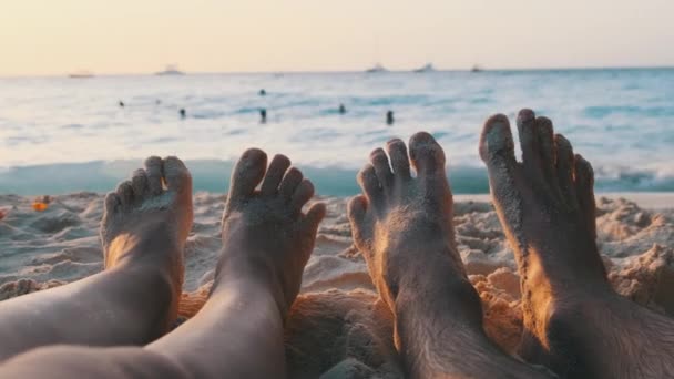 POV Feet of a Couple of Men and Women Leżący na piaszczystej plaży o zachodzie słońca nad oceanem — Wideo stockowe