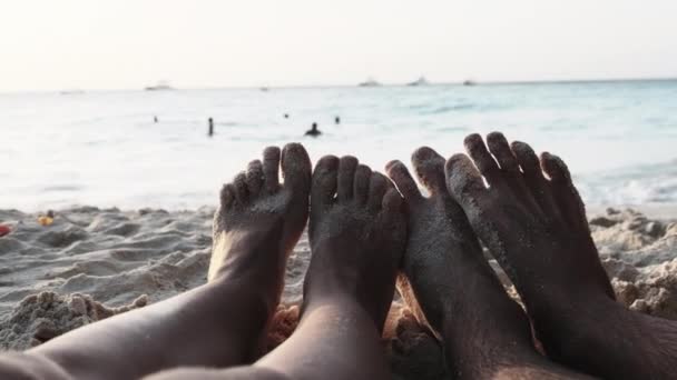 POV Feet of a Couple of Men and Women Leżący na piaszczystej plaży o zachodzie słońca nad oceanem — Wideo stockowe