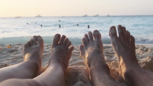 POV Feet of a Couple of Men and Women Leżący na piaszczystej plaży o zachodzie słońca nad oceanem — Wideo stockowe