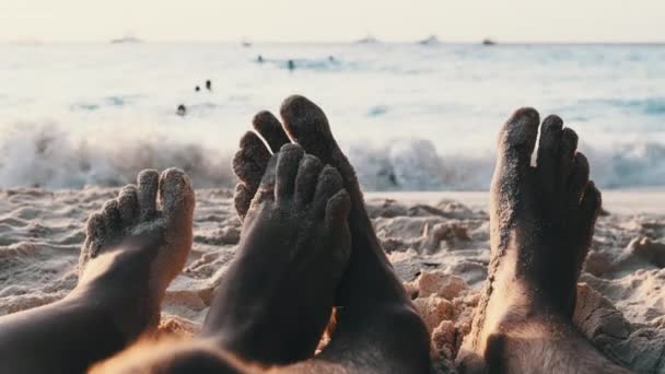 POV Feet of a Couple of Men and Women Leżący na piaszczystej plaży o zachodzie słońca nad oceanem — Wideo stockowe