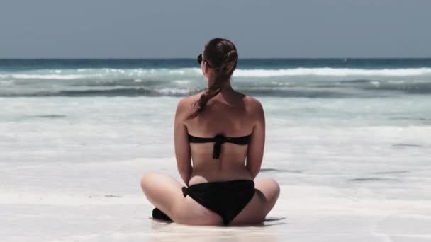 Jonge vrouw in zwarte bikini tinten in Lotus Pose op Paradise Sandy Beach door Ocean — Stockvideo