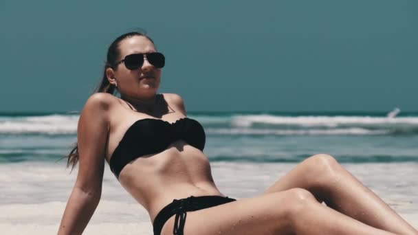 Молода жінка в чорному Бікіні Танс на білому піщаному пляжі Раю лежить біля океану — стокове відео