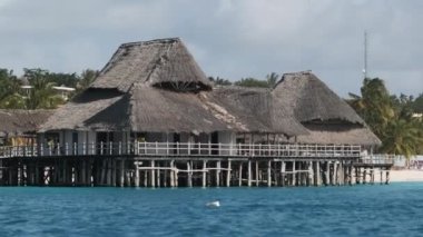 Okyanusun yukarısındaki tahta kutuplarda Thatched Damlı Afrika Restoranı. Zanzibar