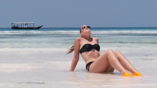 パラダイスの黒ビキニタンズの若い女性白い砂浜は海に横たわっています — ストック動画