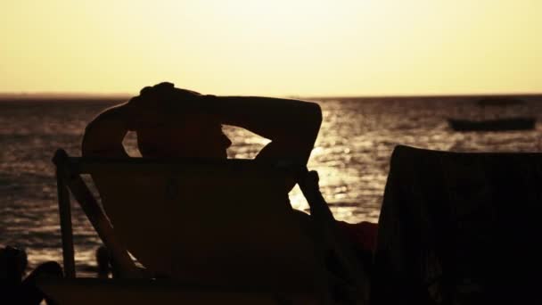 Silhouette de l'homme allongé sur une chaise longue Regardant le coucher du soleil sur l'océan, Zanzibar — Video