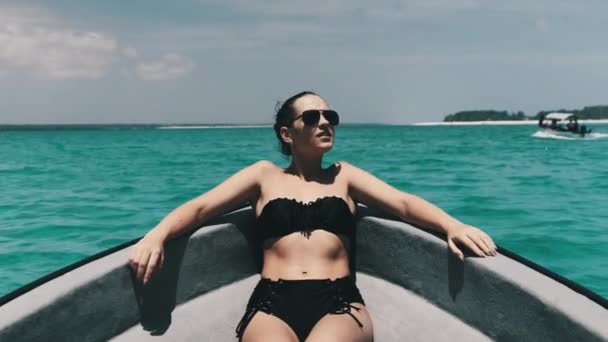 Fiatal nő bikiniben és napszemüvegben fekszik az óceánon úszó hajó orrán. — Stock videók