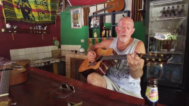 एक वृद्ध अमेरिकन झिंझिबेरियाच्या बाहेरच्या स्थानिक आफ्रिकन बारमध्ये गिटार वाजवते — स्टॉक व्हिडिओ