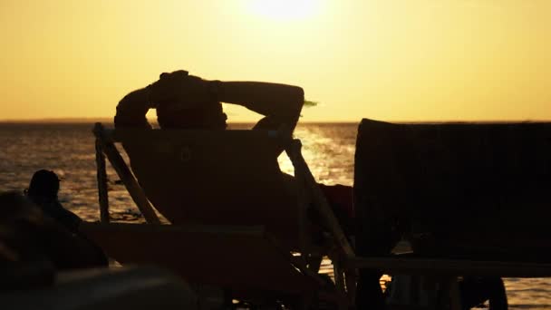 Silhouet van de mens liggend op de ligstoel kijkend naar de zonsondergang door de oceaan, Zanzibar — Stockvideo