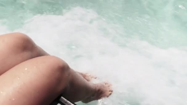 Młoda kobieta Nogi wiszące nad krawędzią pokładu łodzi, dotyk turkusowej wody w oceanie — Wideo stockowe