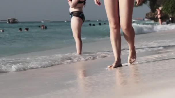 Piernas de una mujer joven caminando por la arena blanca y olas de surf de la orilla del mar — Vídeos de Stock