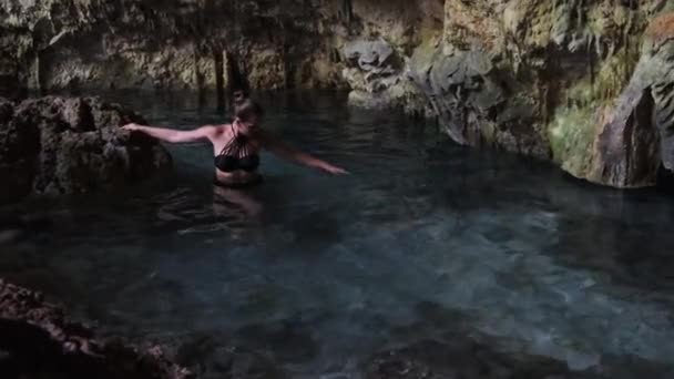 Jeune femme nage dans une rivière souterraine dans une grotte avec de l'eau douce parmi les falaises — Video