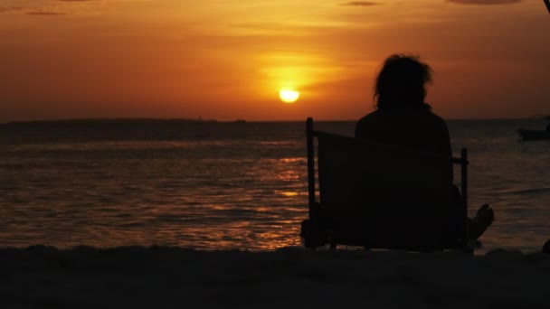 Sylwetka kobiety leżącej na leżaku Patrząc na zachód słońca nad oceanem, Zanzibar — Wideo stockowe