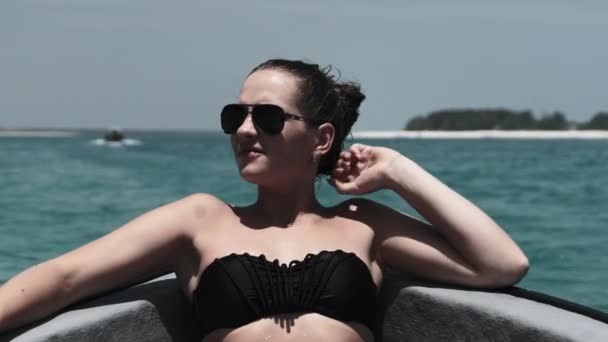 Bikini 'li ve güneş gözlüklü genç kadın Okyanusta yüzen teknenin yayında yatıyor. — Stok video