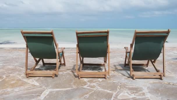 Trois chaises longues vides se tiennent dans une rangée par l'océan sur la plage tropicale, vue arrière — Video