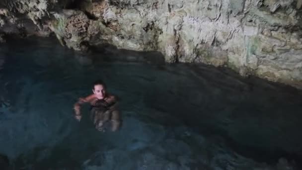 Jeune femme nage dans une rivière souterraine dans une grotte avec de l'eau douce parmi les falaises — Video