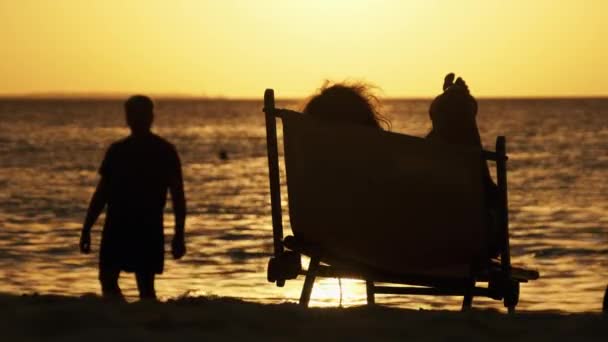 Silhouet van de vrouw liggend op de ligstoel kijkend naar zonsondergang door de oceaan, Zanzibar — Stockvideo