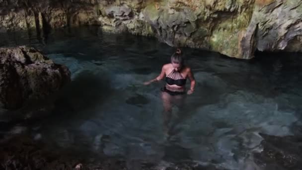 Молода жінка плаває в підземній річці в печері з свіжою водою серед скель — стокове відео