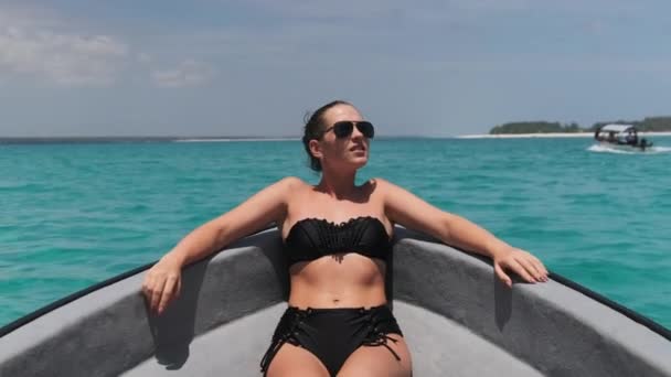 Jovem mulher de biquíni e óculos de sol jaz no arco do barco flutuando pelo oceano — Vídeo de Stock
