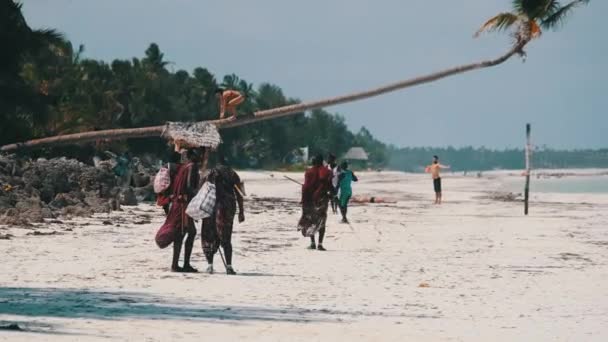 ザンジバル島の観光客の間で海によって熱帯ビーチに沿ってMaasai歩く — ストック動画