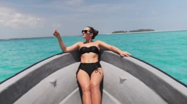 Bikini 'li ve güneş gözlüklü genç kadın Okyanusta yüzen teknenin yayında yatıyor.