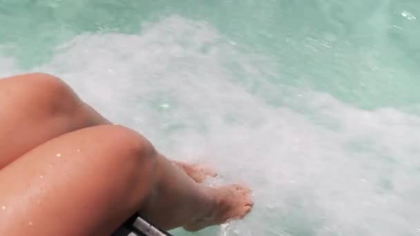Jonge vrouw voeten hangen over de rand van de boot dek, aanraken turquoise water in de oceaan — Stockvideo