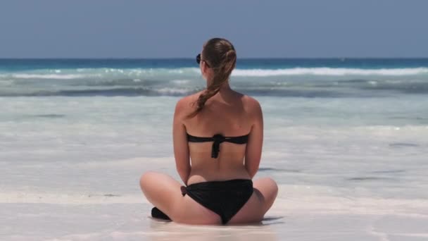 Mulher jovem de biquíni preto Tans in Lotus Pose on Paradise Sandy Beach by Ocean — Vídeo de Stock