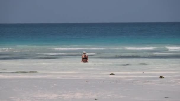 Mujer joven en traje de baño negro entra en el océano Turquesa en Paradise Beach — Vídeo de stock