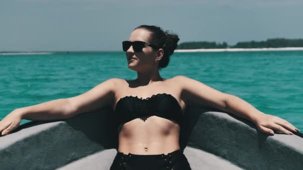 Bikini 'li ve güneş gözlüklü genç kadın Okyanusta yüzen teknenin yayında yatıyor. — Stok video
