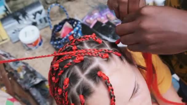 Proceso de tejer trenzas africanas con Kanekalon rojo al aire libre, Zanzíbar, África — Vídeo de stock