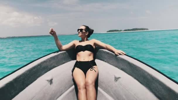 Mujer joven en bikini y gafas de sol se encuentra en el arco del barco flotando por el océano — Vídeos de Stock