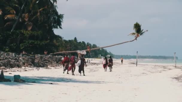 ザンジバル島の観光客の間で海によって熱帯ビーチに沿ってMaasai歩く — ストック動画