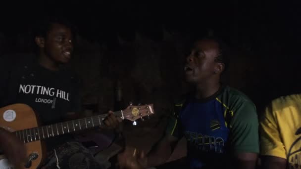Jóvenes africanos locales tocan la guitarra con djembe, cantan canciones alrededor de fogata, noche — Vídeo de stock