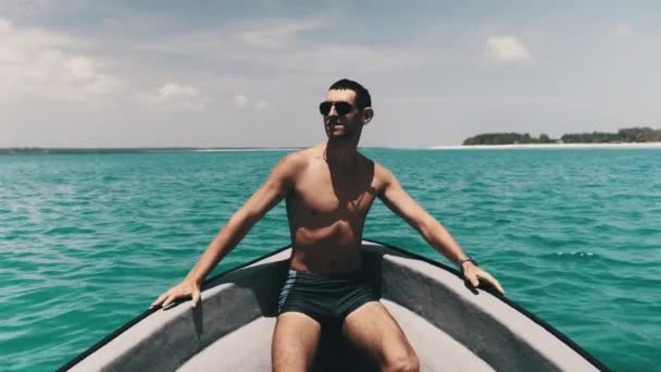 Giovane uomo di successo in occhiali da sole godendo sull'arco della barca galleggiante dall'oceano — Video Stock