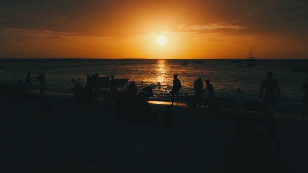 Silhouetten von Menschen bei Sonnenuntergang, die sich am Strand am Meer ausruhen, Sansibar — Stockvideo