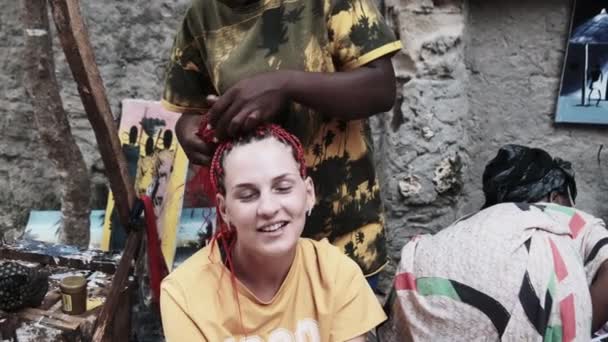 Mulher Africana tecendo tranças africanas com Kanekalon vermelho ao ar livre, Zanzibar África — Vídeo de Stock