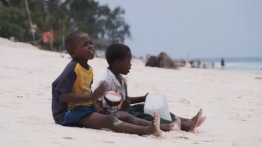 İki Afrikalı çocuk sahilde oturur ve doğaçlama davul çalar, Zanzibar