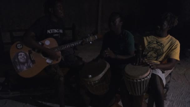 Jóvenes africanos locales tocan la guitarra con djembe, cantan canciones alrededor de fogata, noche — Vídeos de Stock